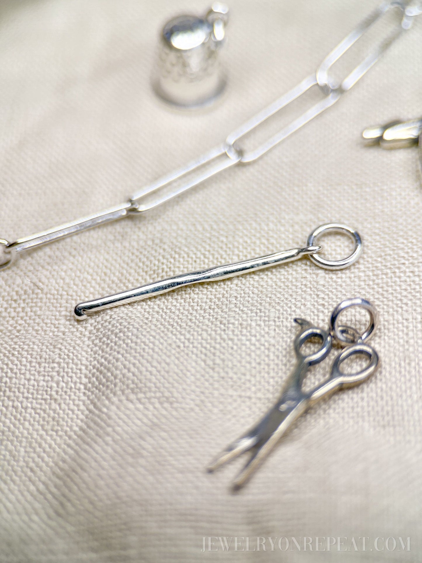 May include: Silver charm necklace with a silver thimble charm, a silver scissors charm, and a silver knitting needle charm.