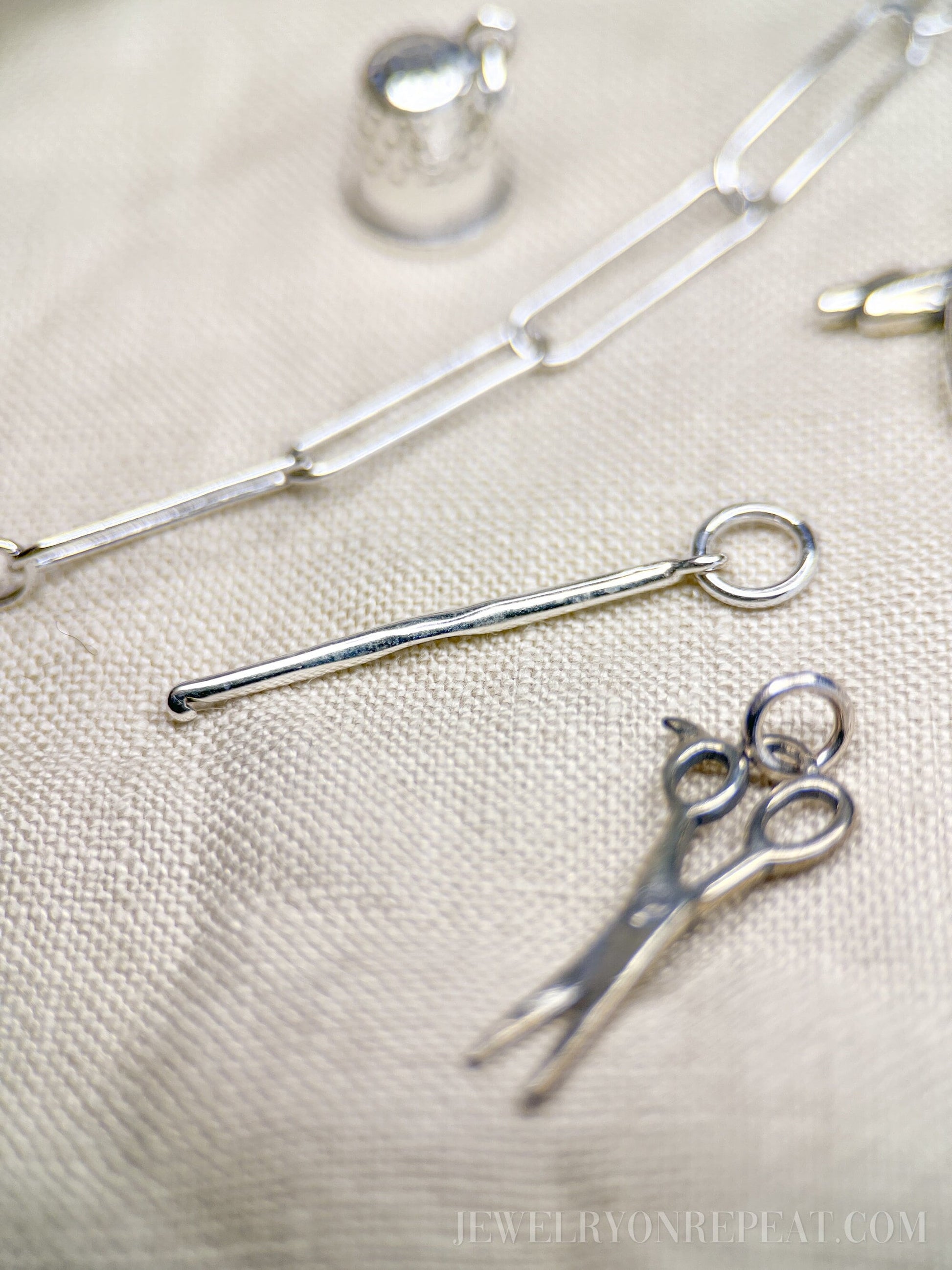 May include: Silver charm necklace with a silver thimble charm, a silver scissors charm, and a silver knitting needle charm.
