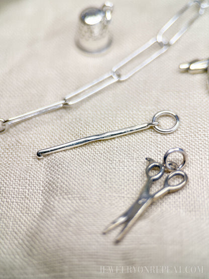 May include: Silver charm necklace with a silver thimble charm, a silver scissors charm, and a silver knitting needle charm.