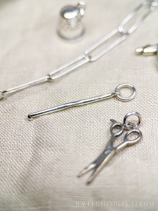 May include: Silver charm necklace with a silver thimble charm, a silver scissors charm, and a silver knitting needle charm.