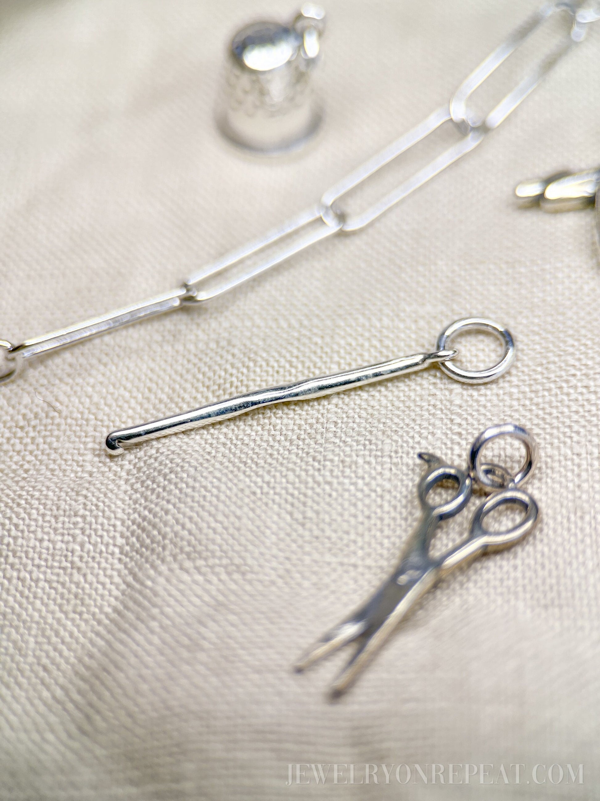 May include: Silver charm necklace with a silver thimble charm, a silver scissors charm, and a silver knitting needle charm.