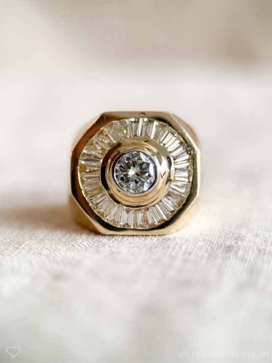May include: A gold ring with a large round diamond in the center surrounded by smaller baguette diamonds.