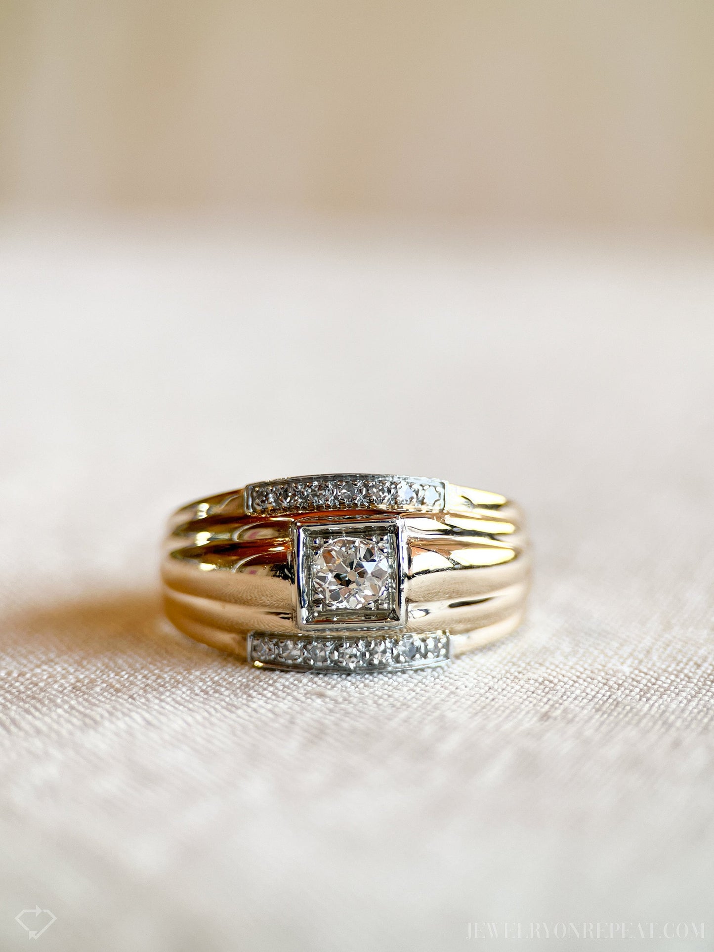 May include: A gold band ring with a square-shaped center stone and smaller diamonds set in the band.