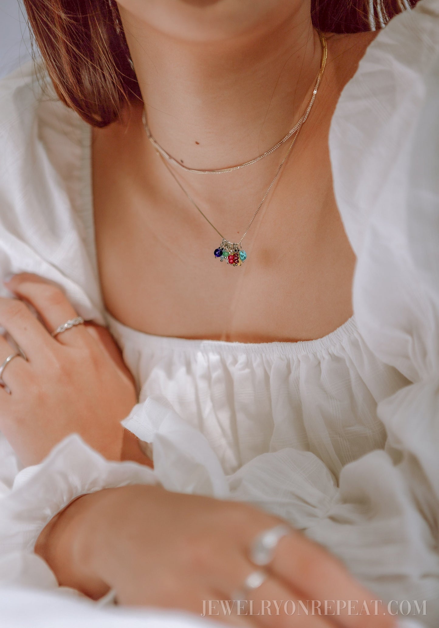 May include: A silver chain necklace with a charm featuring multiple colorful gemstones. The necklace is layered over a thin silver chain.