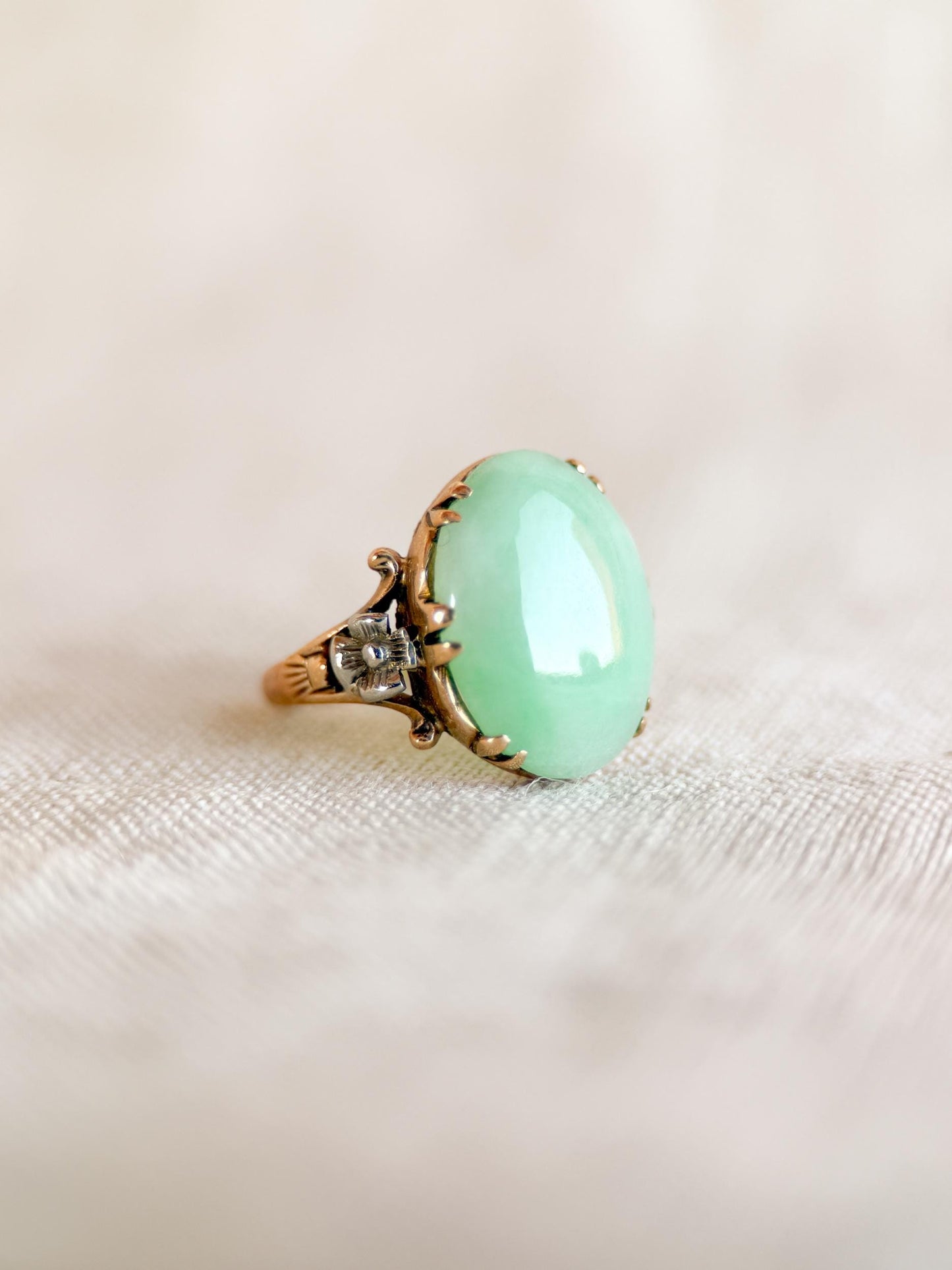 May include: A vintage ring featuring a large, oval-shaped, pale green gemstone set in a gold-toned filigree setting. The ring has intricate floral detailing on the band and around the stone, showcasing a classic, elegant design.