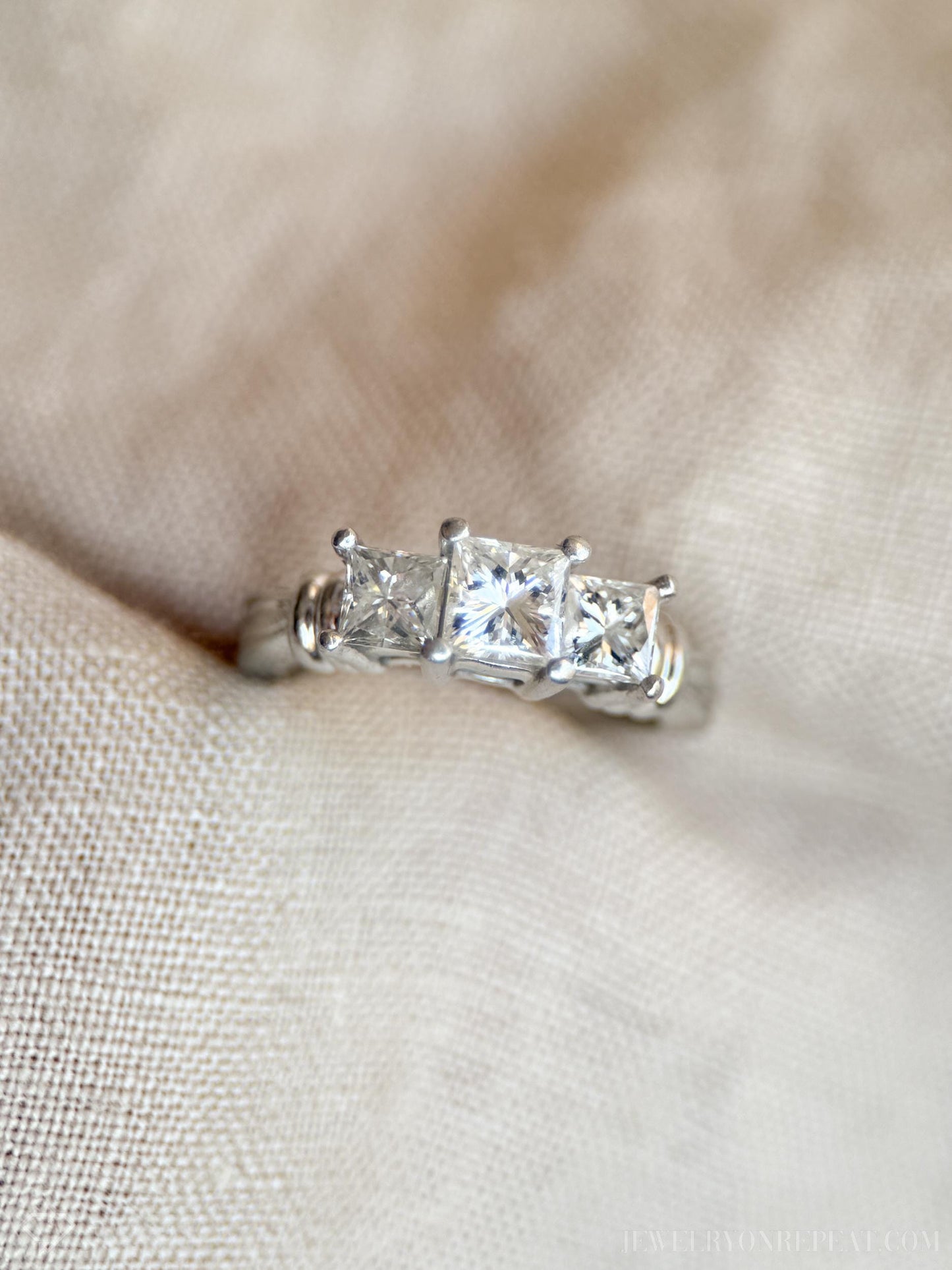 May include: A silver ring with three princess-cut diamonds. The center diamond is larger than the two diamonds on either side.